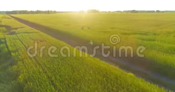 鸟瞰年轻男孩骑着自行车穿过古老的乡村道路上的麦田阳光和光束视频的预览图