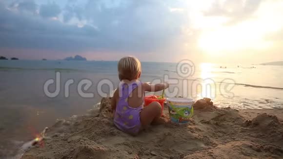穿紫色泳装的小女孩在沙滩上玩耍视频的预览图