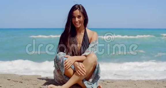 微笑迷人的女人坐在沙滩上视频的预览图