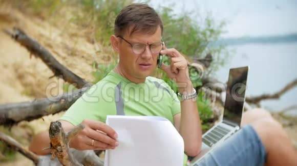 忙碌的成熟的男人在一台手提电脑上工作手里拿着打电话坐在海滩上视频的预览图
