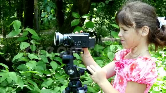 年轻女孩在绿色公园背景下看摄像机视频的预览图