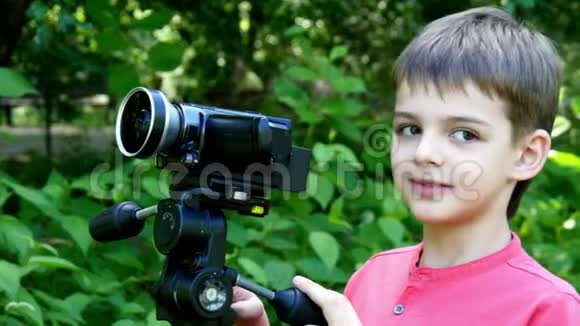 小男孩看着绿色公园背景上的摄像机视频的预览图