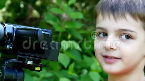 小男孩看着绿色公园背景上的摄像机视频的预览图