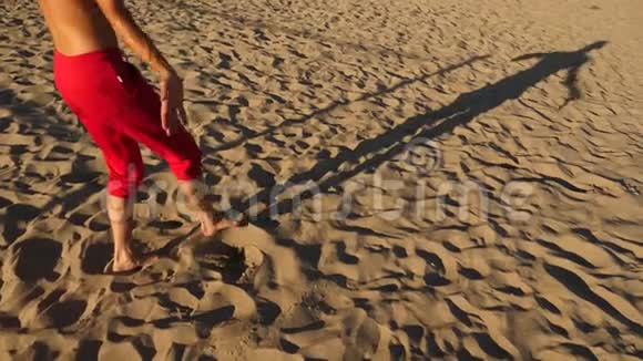 一个年轻快乐的家伙跳着现代芭蕾在海边的沙滩上打盹缓行视频的预览图