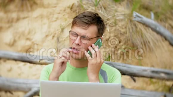 忙碌的成熟的男人在一台手提电脑上工作手里拿着打电话坐在海滩上视频的预览图