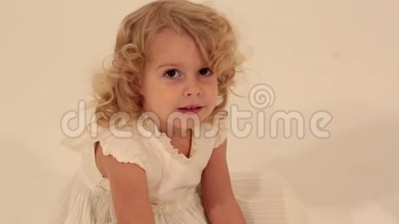 可爱的小可爱的幼儿女孩一头金发穿着白色连衣裙看着镜头挥手告别视频的预览图
