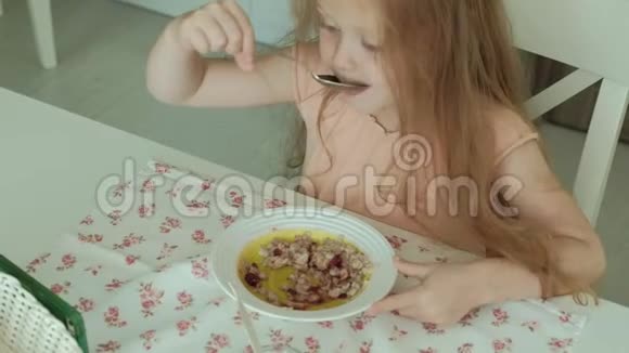 快乐的美丽女孩早餐吃粥在家的白色厨房里玩得开心视频的预览图