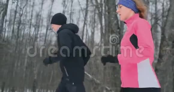 冬天早晨一对年轻健康的年轻夫妇穿着运动服在森林里奔跑视频的预览图