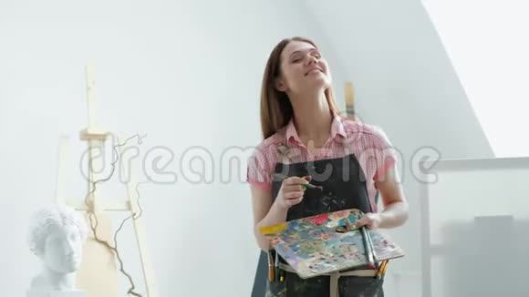 年轻美丽的女画家在画架和画布在一个明亮的工作室视频的预览图