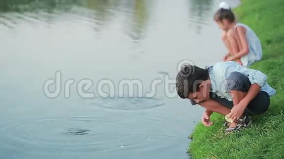 穿着粉红色衣服在花园池塘里喂鱼的小女孩湖边的孩子视频的预览图