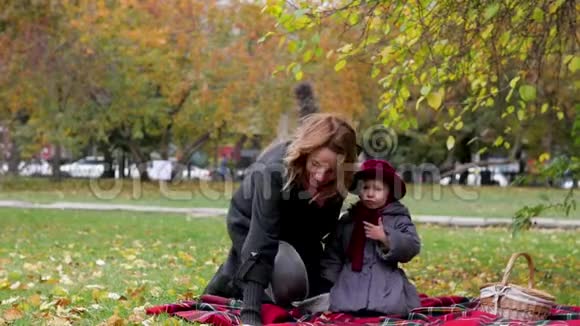 妈妈和女儿在公园里玩耍躺在地毯上扔树叶视频的预览图