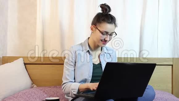 一个年轻漂亮的女孩正在家里的床上用她的笔记本电脑工作视频的预览图