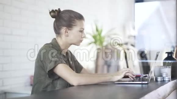 穿绿色衬衫的年轻女子在笔记本电脑上打字视频的预览图