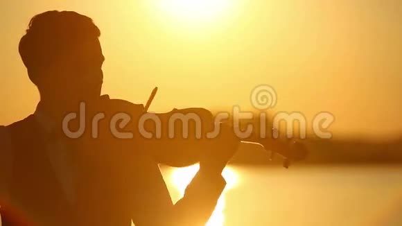 日落时分男小提琴手在湖边拉小提琴视频的预览图