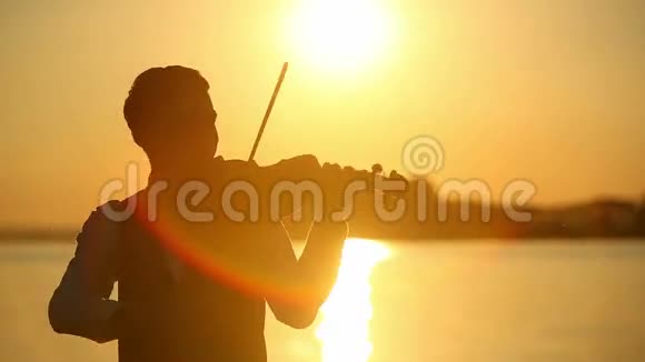 日落时分男小提琴手在湖边拉小提琴视频的预览图