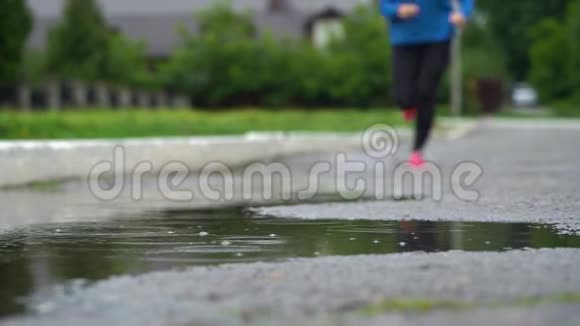 穿运动鞋的跑步者的腿运动女人在户外慢跑踩在泥泞的水坑里单跑运动员在雨中奔跑视频的预览图