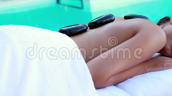 安静的黑发女人在泳池边做热石按摩视频的预览图