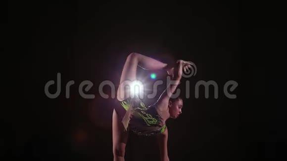 穿着色彩鲜艳的泳衣的可爱女孩运动员在黑暗的健身房里表演艺术体操元素视频的预览图