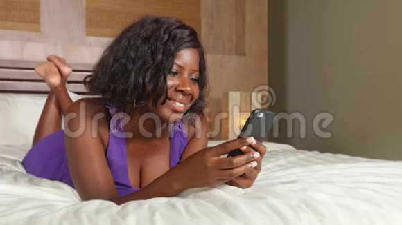 年轻美丽快乐的黑人非裔美国妇女坐在床上用互联网手机微笑轻松的网络上网视频的预览图