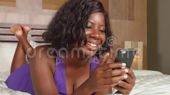 年轻美丽快乐的黑人非裔美国妇女坐在床上用互联网手机微笑轻松的网络上网视频的预览图