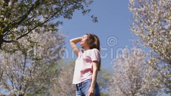 成功的商务女性在公园里享受休闲的自由时光樱花盛开穿着牛仔裤粉红色的樱花树视频的预览图