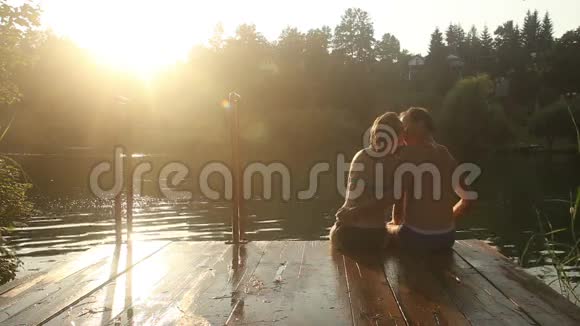 日落时分浪漫的情侣坐在河边接吻视频的预览图