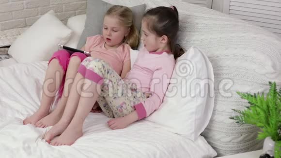 可爱的小女孩躺在床上使用数字平板电脑视频的预览图