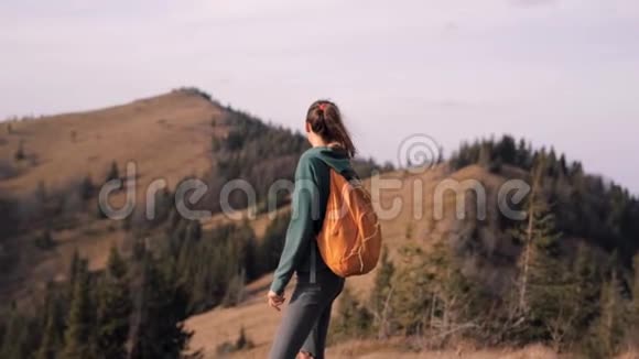 在日落的背景下站在山脊边缘的女徒步旅行者视频的预览图
