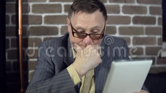 戴眼镜的高级商人正在办公室里用一台数码平板电脑视频的预览图