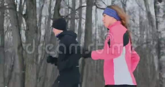 冬天早晨一对年轻健康的年轻夫妇穿着运动服在森林里奔跑视频的预览图