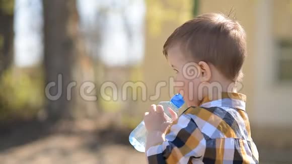 阳光明媚的一天英俊的男孩从瓶子里喝清水视频的预览图