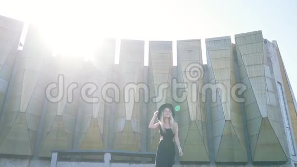 在城市建筑背景下美丽的时尚女孩穿着黑色连衣裙在镜头前摆姿势微笑视频的预览图