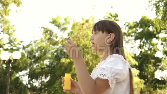 美丽的女孩在春天夏天和微笑的公园里吹肥皂泡慢动作年轻女孩在玩视频的预览图