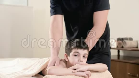 男性理疗师按摩师为躺在按摩床上的小男孩做一个疗愈放松的按摩手和手视频的预览图