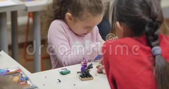 坐在书桌前的可爱的小孩子们在桌子上雕刻出了一与彩色造型塑料制成的不同的图形视频的预览图