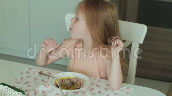 快乐的美丽女孩早餐吃粥在家的白色厨房里玩得开心视频的预览图
