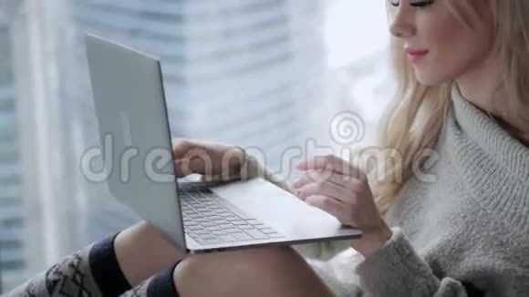 美丽的金发女人坐在床上带着灰色的铝制笔记本电脑女孩微笑心情好博客浏览互联网视频的预览图