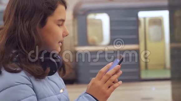 十几岁的女孩带着智能手机和耳机等待地铁很多人聚集在地下地下地铁公司视频的预览图