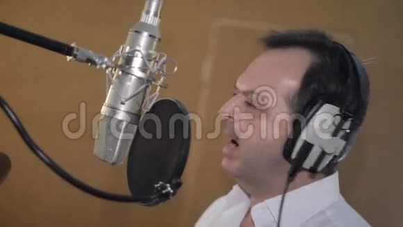 穿白色衬衫的人在麦克风前的耳机里唱歌的肖像工作室视频的预览图