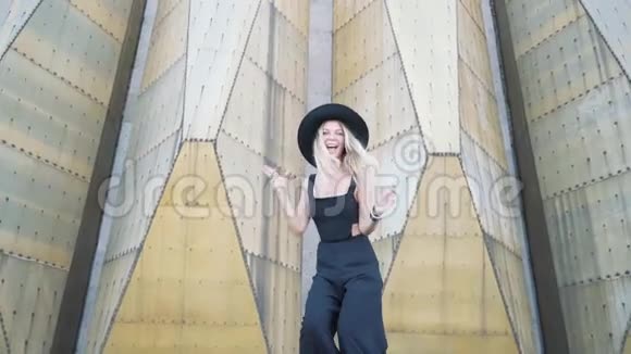 在城市建筑背景下美丽的时尚女孩穿着黑色连衣裙在镜头前摆姿势微笑视频的预览图