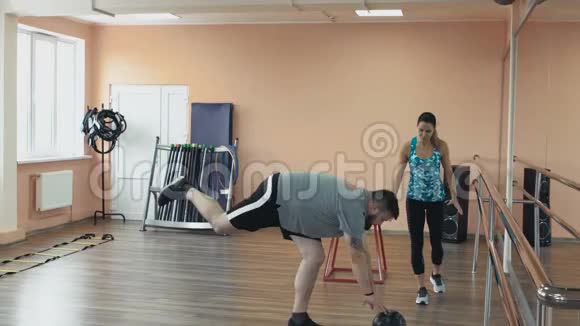 胖子和女教练一起训练在健身中心做运动厚肥胖的家伙和个人视频的预览图