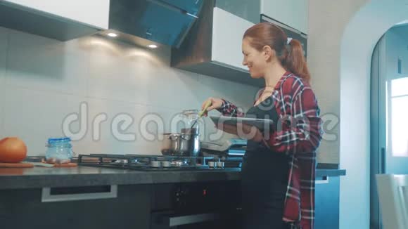 女人在厨房煮汤锅防止锅里的水看看数字平板上的食谱妇女视频的预览图
