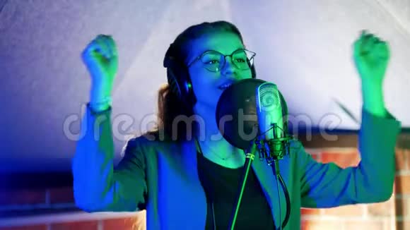 一个戴着眼镜和耳机在工作室唱歌的年轻女人霓虹灯照明视频的预览图