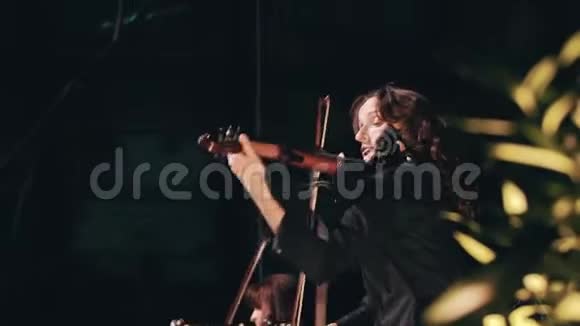 美丽的女孩小提琴手穿着黑色的衣服和长长的卷发在舞台上拉小提琴很酷的女音乐家摇滚乐队视频的预览图