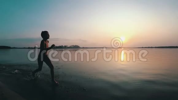 快乐男孩在日落时沿着海滩奔跑慢动作视频的预览图