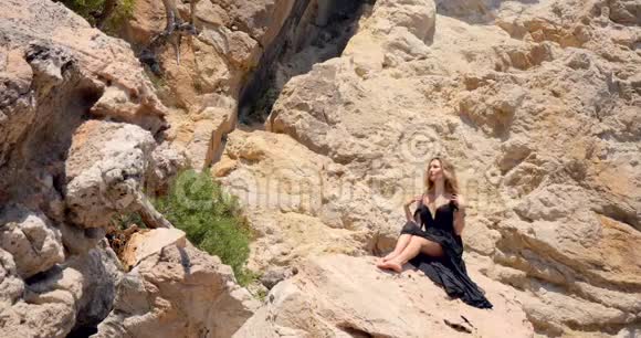 美丽的女人穿着优雅的黑色裙子在岩石上视频的预览图
