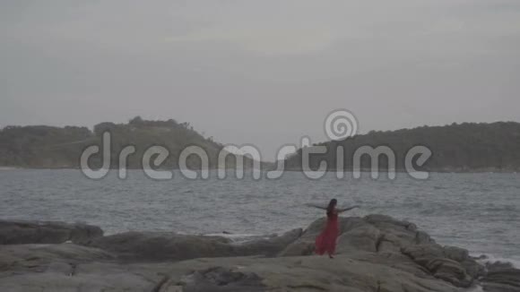 美丽迷人的女人穿着红裙子在海边的岩石上尽情享受视频的预览图
