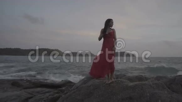 美丽迷人的女人穿着红裙子在海边的岩石上尽情享受视频的预览图