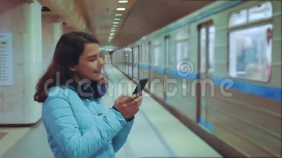少女在地下地铁里乘地铁等待火车的到来手持智能手机小女孩视频的预览图