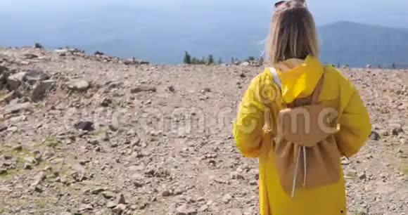 徒步旅行者背着背包在山顶徒步旅行穿着黄色雨衣的女孩在山顶上视频的预览图